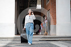 Asian woman tourist talking on smartphone while walking to dragging with black luggage to passengers lounge