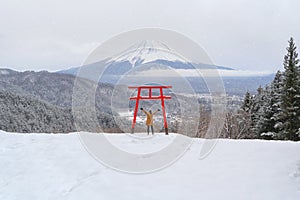 Asian woman tourist travel at Red Japanese Torii pole, Fuji mountain and snow in Kawaguchiko, Japan. Forest trees nature landscape