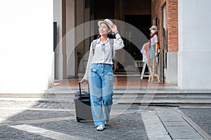 Asian woman tourist is traveling on holiday trip with hat and dragging her black luggage