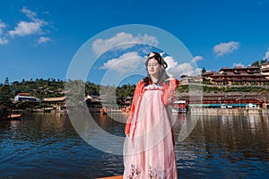 Asian woman tourist wearing red Hanfu ancient Chinese traditional dress standing on wooden boat at reservoir of Ban Rak Thai