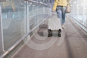 Asian woman traveler dragging carry on luggage suitcase at airport corridor walking to departure gates