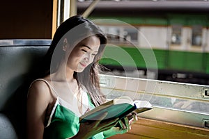 Asian woman traveler has reading a book in the train with happiness at Hua Lamphong station at Bangkok, Thailand.