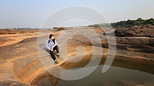 Asian woman traveler hiking in rock mountain and stopped to have rest near the lake pond on the peak of hill