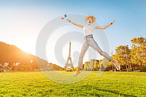 Asian woman traveler jumping with french flag at Mars Field at the background of majestic Eiffel tower. Tourism and
