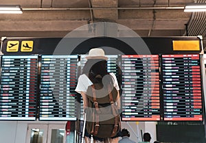 Asian woman traveler looking information board with carrying, suitcase