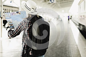 Asian woman travelers with backpacking, see map in the railway station, planning a tour, with train parked in station, concept