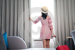 Asian woman traveller in pink dress arrive to room in hotel and open curtain photo