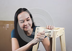 Asian woman  trying to assemble knockdown furniture, screwing the screw into wood and smiling