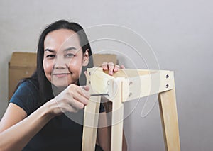 Asian woman  trying to assemble knockdown furniture, screwing the screw into wood and smiling and looking at camera