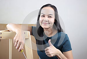 Asian woman  trying to assemble knockdown furniture, showing her thumb up and smiling at camera