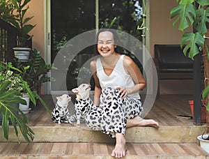Asian woman and two chihuahua dogs wearing dalmatian or cow patterned costume, sitting in balcony with houseplant pots, smiling