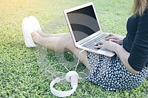 Asian woman typing Thai keyboard of laptop and sitting on green grass by relaxing