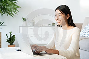 Asian woman typing work with laptop homework, Asia student learning online using computer while sitting at home  morning sunlight
