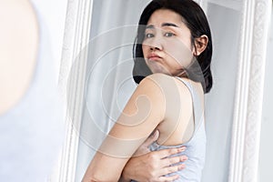 Asian woman unhappy with back bra bulge fat , checking upper back fat in a mirror