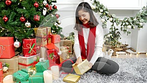 Asian Woman unwrap christmas gift box under xmas tree got surprise present gift.