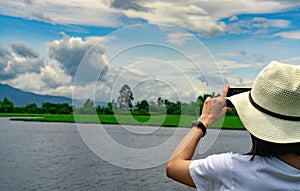 Asian woman use smartphone take a picture of beautiful landscape of river, mountain, and forest. Summer vacation trip. Hipster