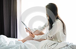 Asian woman use a tablet on the bed after wake up in weekend mornning.Use the tablet to read news, watch movies, or chat in