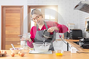 Asian woman using the blender, blend dough and other ingredients for cooking the chocolate cake with happy feeling in the kitchen