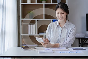 Asian woman using calculator and laptop document for doing financial mathematics on desk, tax, report, home