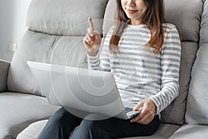 Asian woman using computer and communicates with family on the internet. Girl sitting on sofa at home and video call with friend