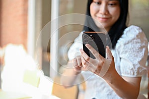 Asian woman using her mobile phone, messaging her friends while chilling at the cafe. cropped