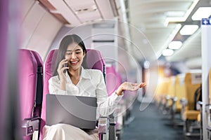 Asian woman using modern smartphone and laptop computer while sitting on airplane Asian woman sitting next to airplane