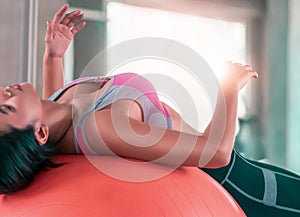 Woman using orange fitness ball to strech her back and exercise her abs in fitness gym workout room