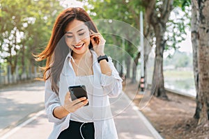 Asian woman using the small talk headphones to make a happy phone call in the park