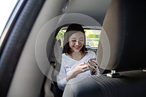 Asian woman using a smartphone in back seat of car.