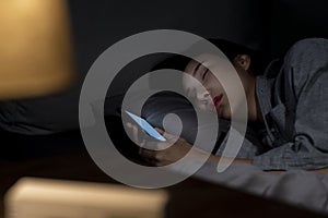 Asian woman using smartphone in bed cannot sleep from insomnia, depressed woman in bedroom