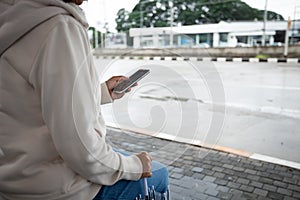 Asian woman is using on smartphone, checking social media network  while waiting taxi at bus stop in rainy day