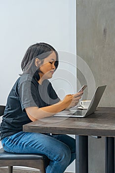 Asian woman using smartphone and laptop at coffeeshop