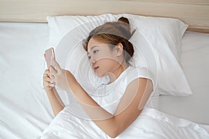 Asian woman is using a smartphone and she is lying on the bed