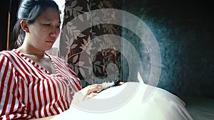 Asian woman using a smartphone while relaxing on bed in the bedroom