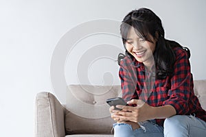 Asian woman  are using a smartphone while on sitting sofa in the living room at home. Woman wearing a red plaid shirt  look