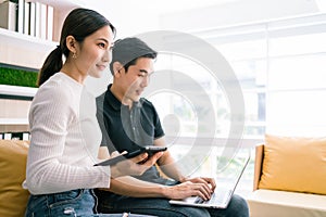 Asian woman using a tablet and looking with confidence, sitting by the man working on the laptop. Casual businesspeople working