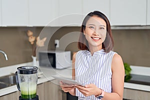 Asian woman using tablet to find recipe making smoothie with fruit and vegetable in kitchen