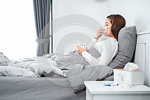Asian woman using tissue to cough, sneeze and holding a glass of water to take medicine while feeling sick