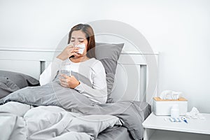 Asian woman using tissue to cough, sneeze and holding a glass of water to take medicine while feeling sick