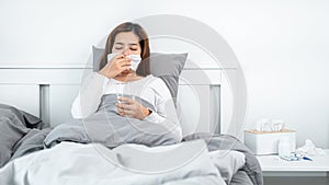 Asian woman using tissue to cough, sneeze and holding a glass of water to take medicine while feeling sick