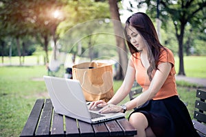 Asian woman using and typing on laptop keyboard in outdoors park