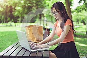 Asian woman using and typing on laptop keyboard in outdoors park. Woman chatting to her friends on social network. People and