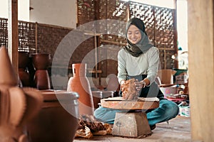 an asian woman in veil makes pottery on a wheel