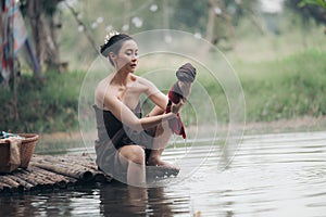 asian woman waering salong sitting on wooden bridge washing clothes in the river