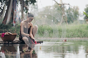 asian woman waering salong sitting on wooden bridge washing clothes in the river