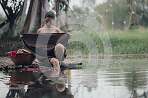 asian woman waering salong sitting on wooden bridge washing clothes in the river