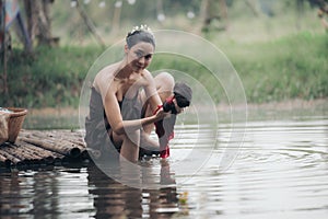 asian woman waering salong sitting on wooden bridge washing clothes in the river