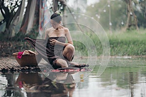 asian woman waering salong sitting on wooden bridge washing clothes in the river