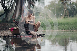 asian woman waering salong sitting on wooden bridge washing clothes in the river