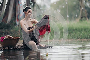 asian woman waering salong sitting on wooden bridge washing clothes in the river